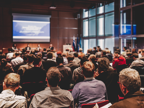 A large audience attentively listens to a panel discussion during an in-person conference event