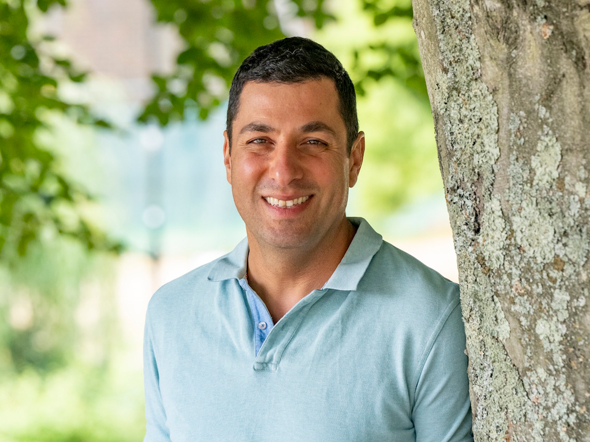 Professor Ali Tavassoli leaning against a tree in pale blue polo shirt