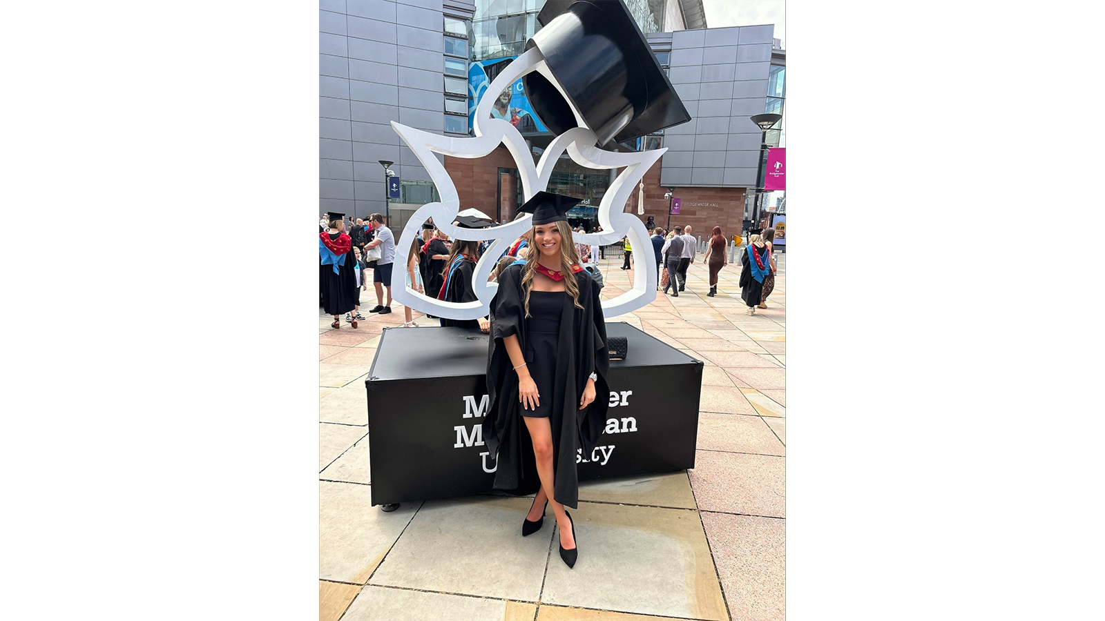 Georgia Wignall in a graduation gown and cap standing in front of a sign