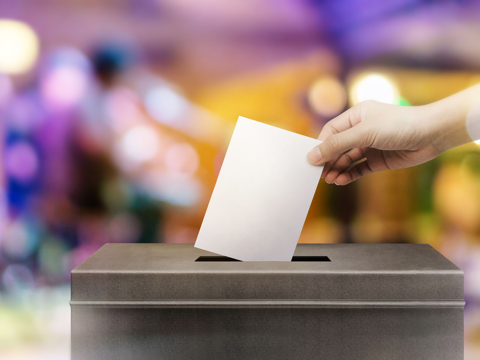 A hand drops a voting slip into a ballot box