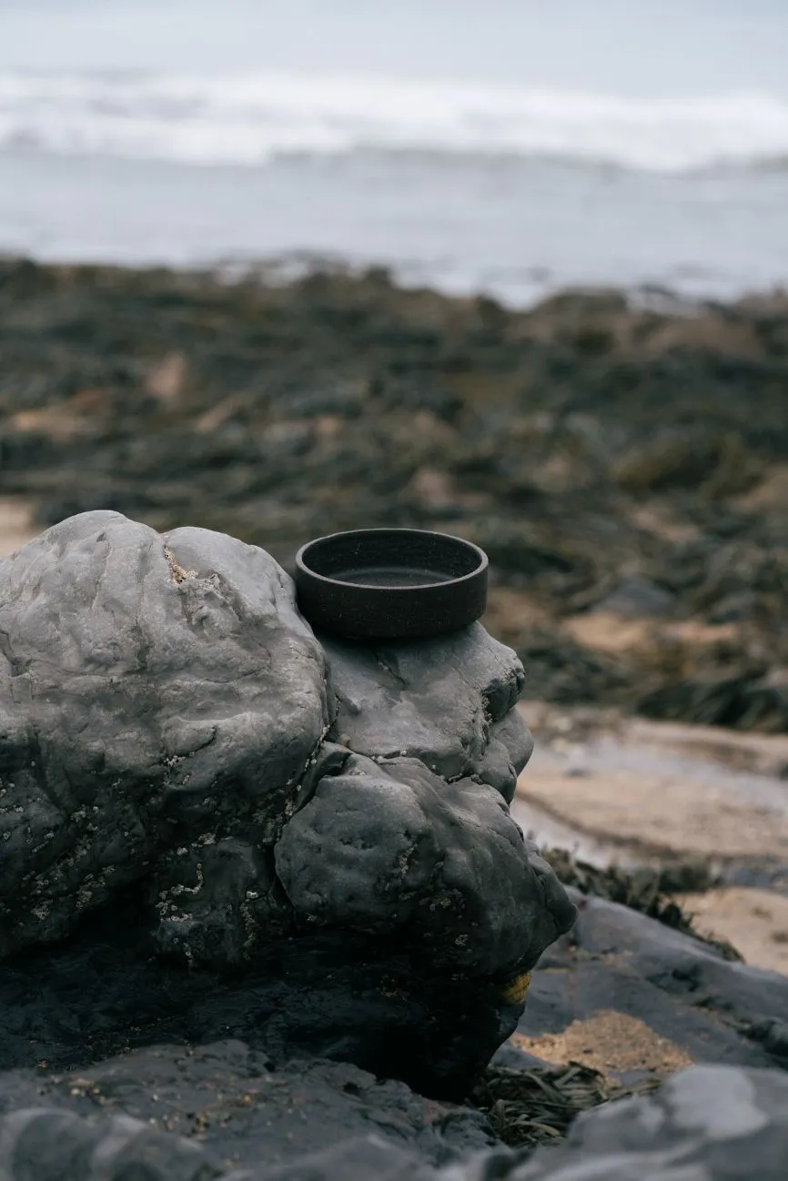 A little container lid made out of Notpla Rigid on a stony beach