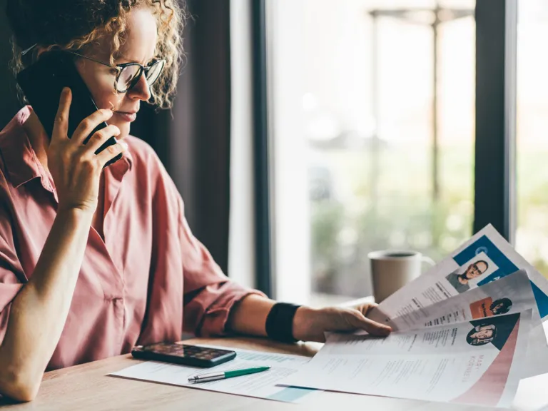 A woman talks on mobile phone looking at many different cv resume