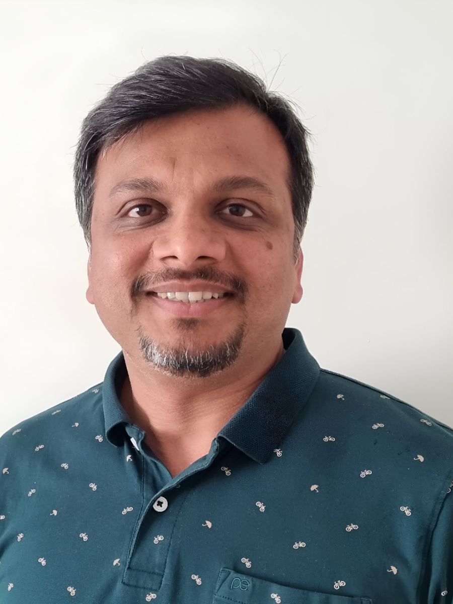 Dr Amit Kumar with moustache and beard, smiling for camera in dark green shirt