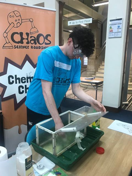 A young man in a blue shirt and safety goggles takes something out of a box.