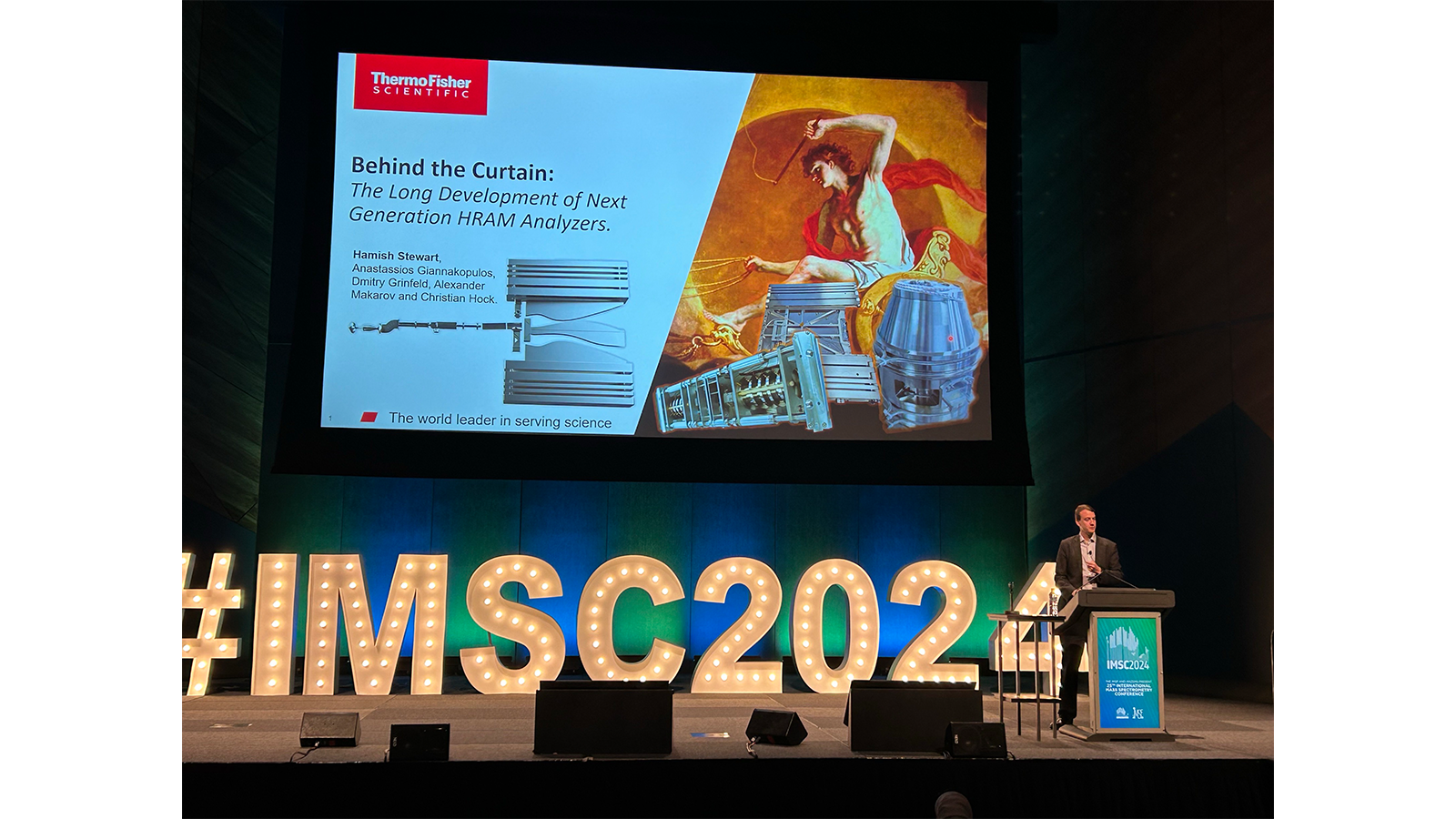 Orbitrap Astral Team member presenting at a podium with a large screen