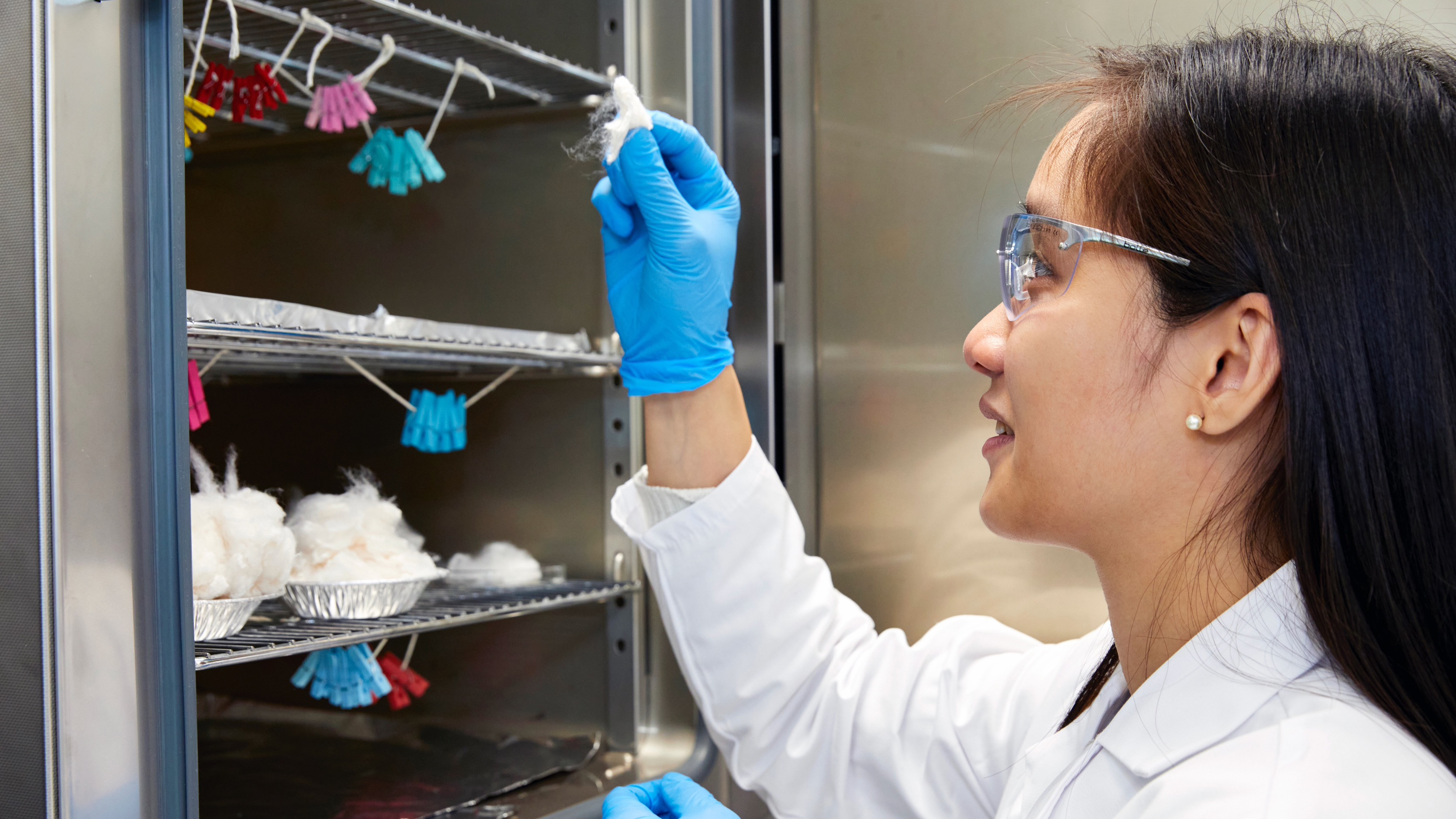 Dr Florence Huynh in a lab coat, gloves and glasses holding material from her research in the lab