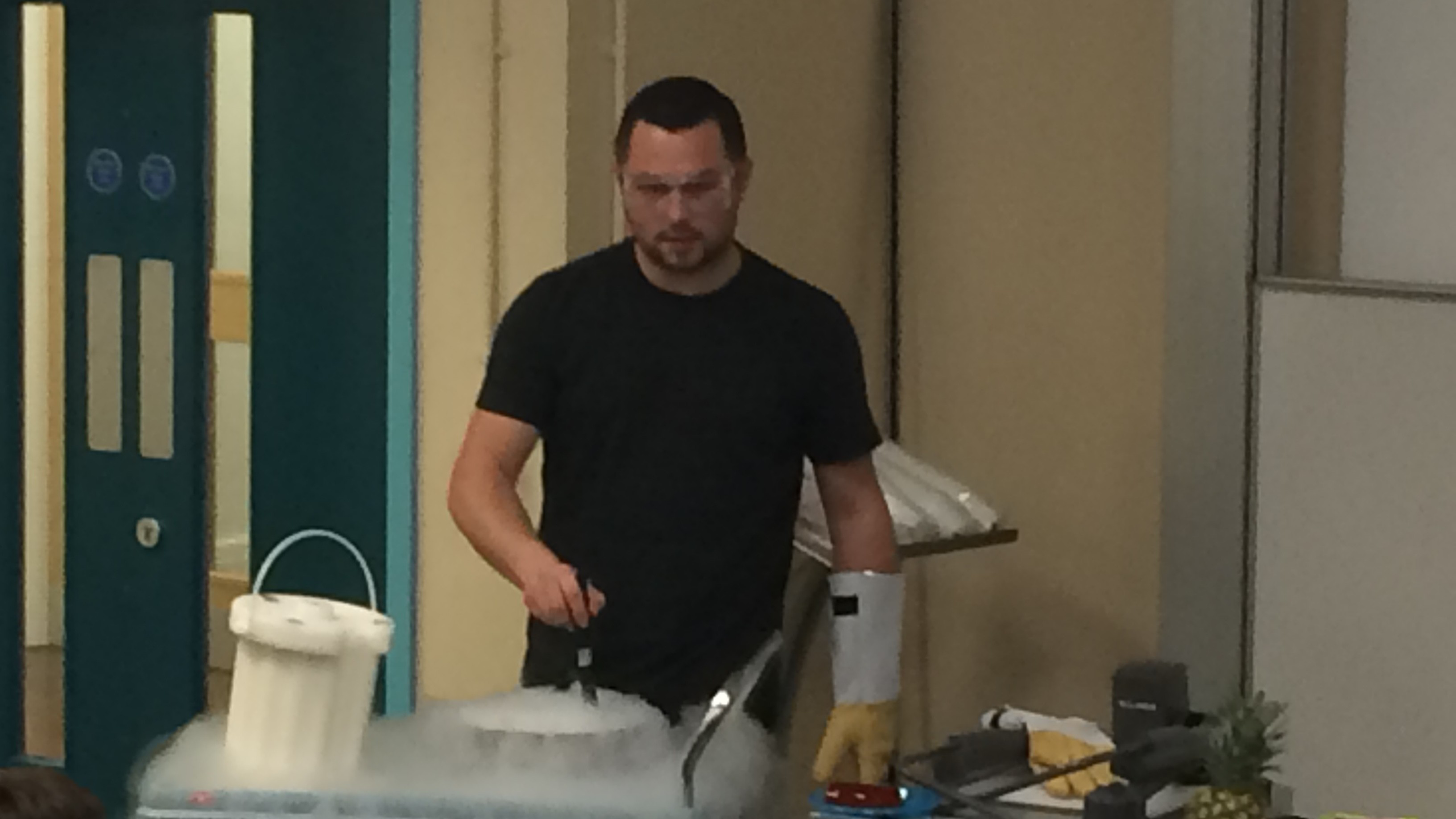 Dr Graeme Turnbull wearing gloves and protective glasses performing an experiment, giving off dry ice