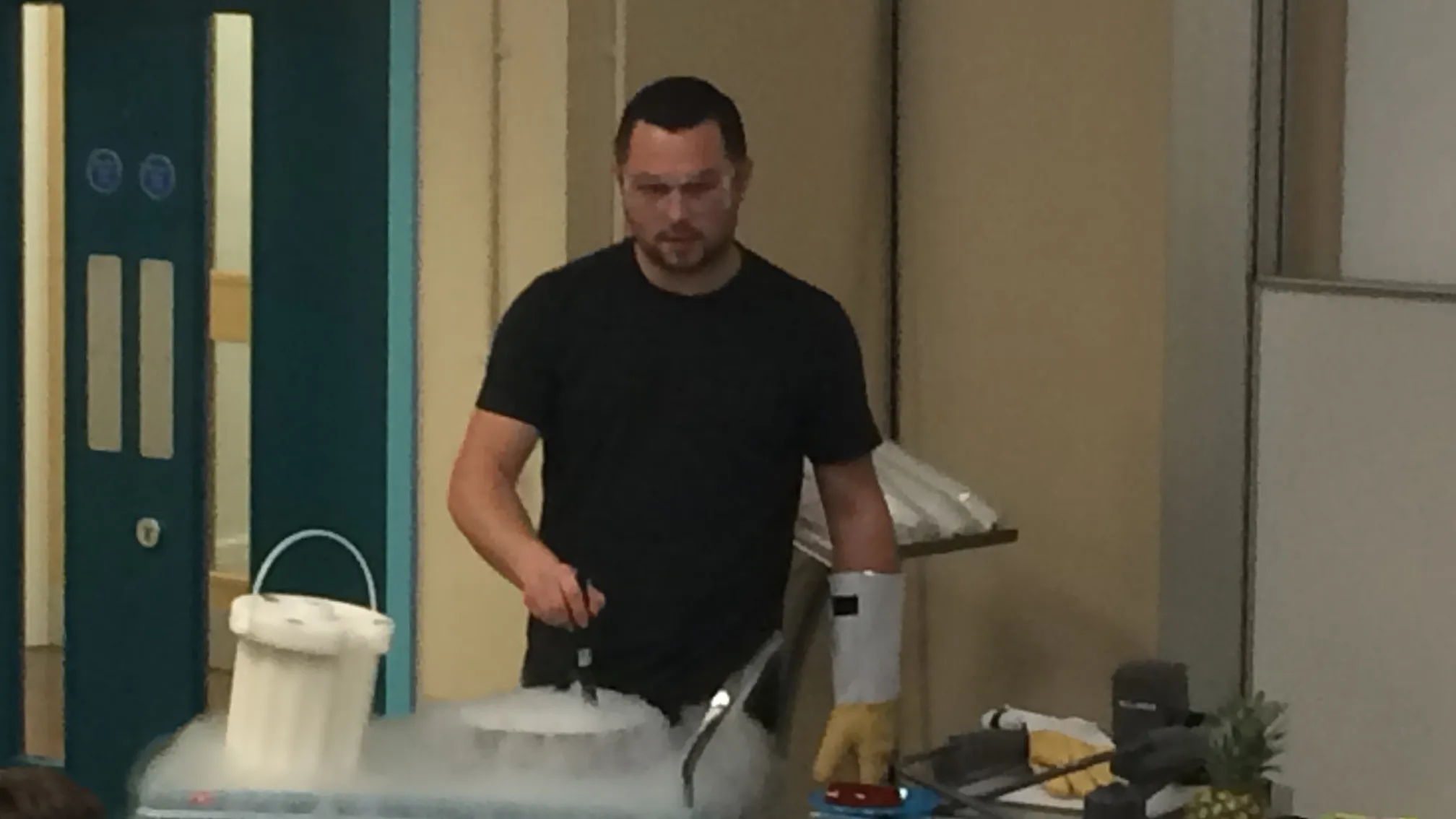 Dr Graeme Turnbull wearing gloves and protective glasses performing an experiment, giving off dry ice